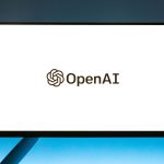 Logo da OpenAI exibido em um monitor diante de um fundo azul em degradê