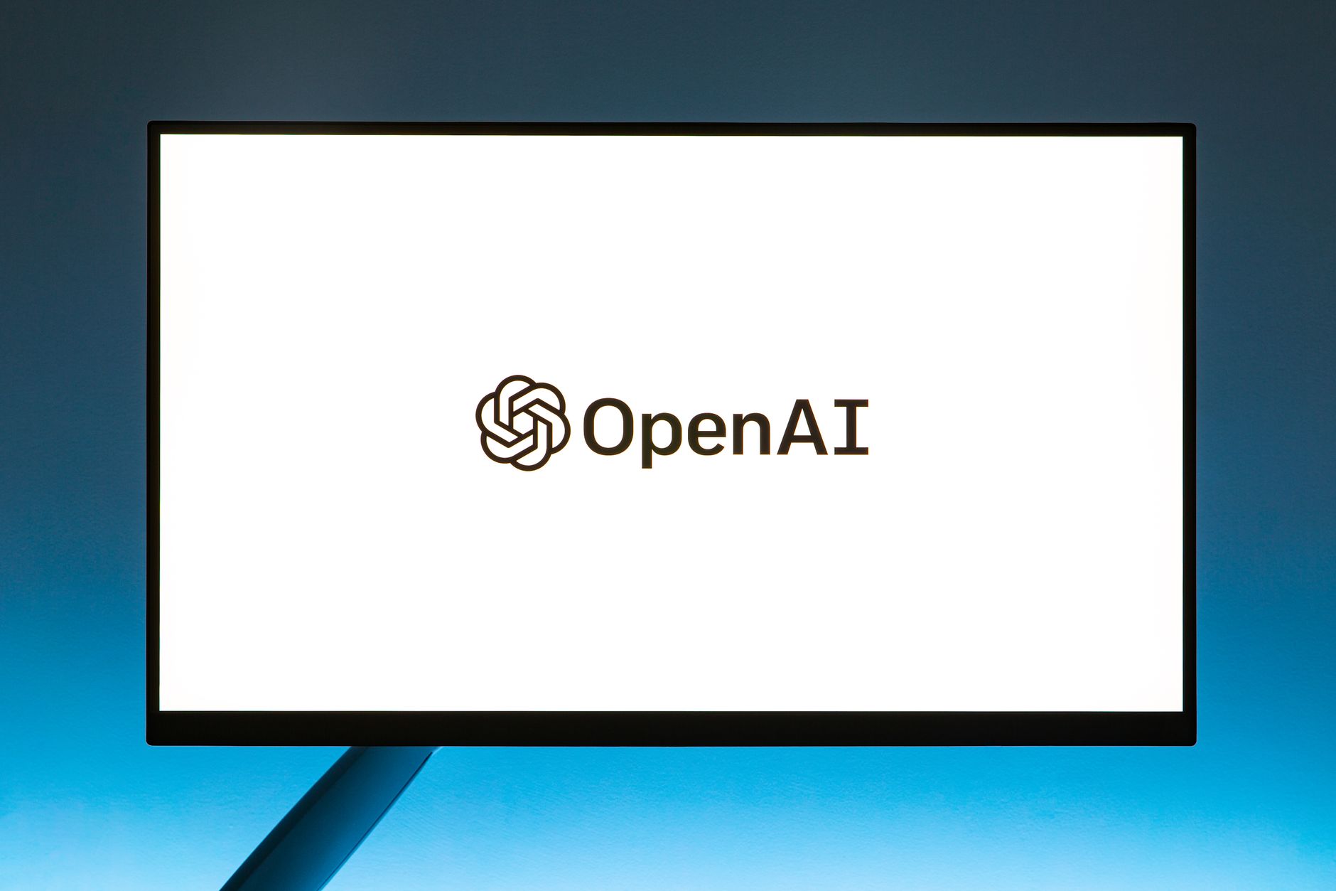Logo da OpenAI exibido em um monitor diante de um fundo azul em degradê