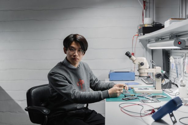 Técnico trabalha com componentes eletrônicos e um microscópio em um laboratório de desenvolvimento de microchips.